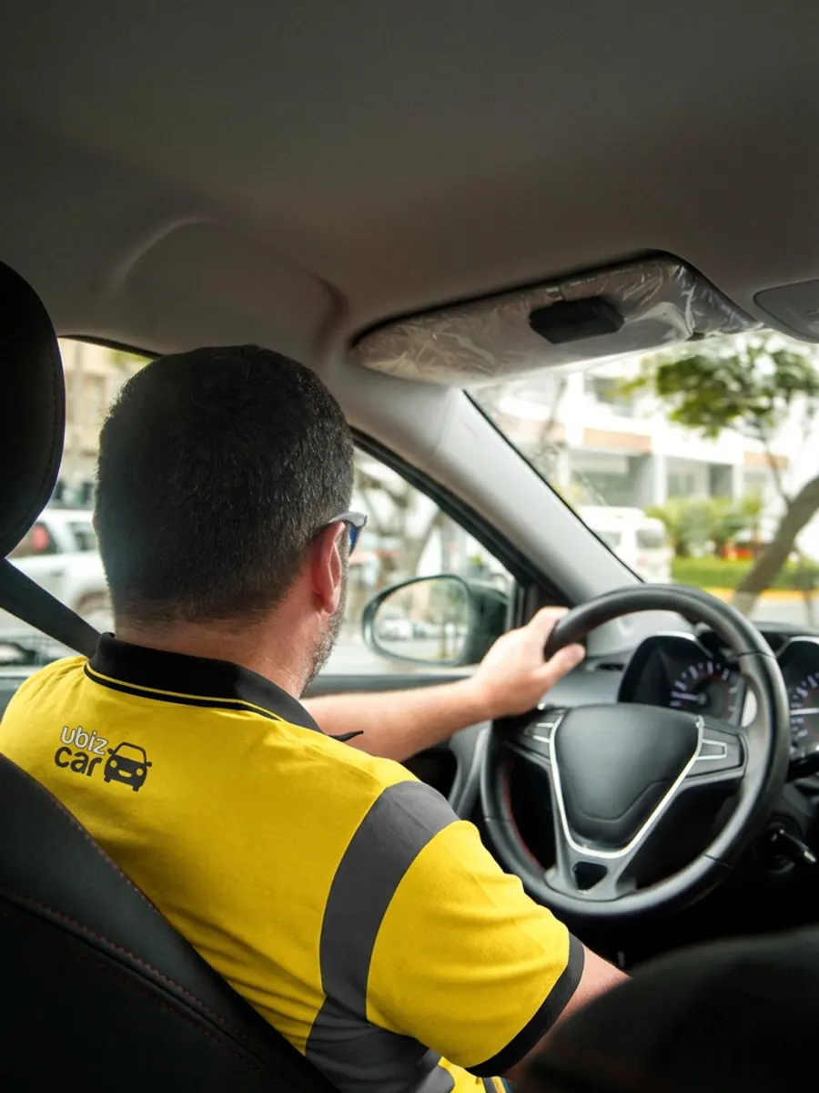 Motorista da Ubiz Car ao volante, visto de trás, com a camisa da marca.